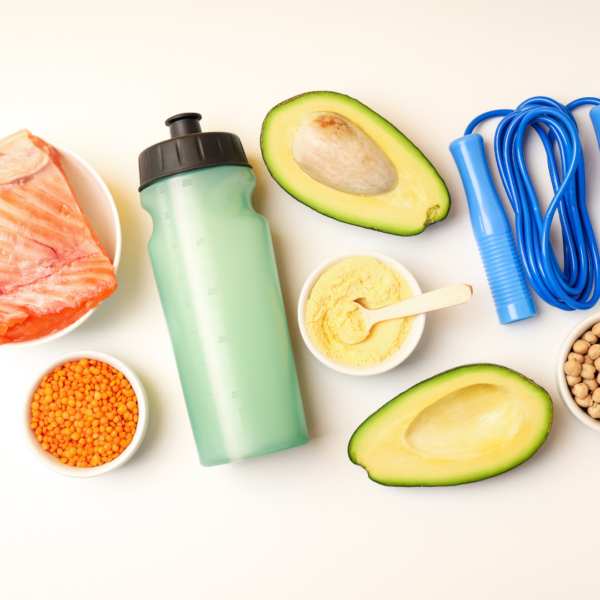 Imagen de productos nutricionales correctos para un entrenamiento o carrera deporitva. Se ve un salmón, legumbres, paltas y pasta de garbanzos. Todas grasas buenas. Además se ve una botella de agua para mantenerse hidratado y una soga de saltar para referir al deporte de cardio.